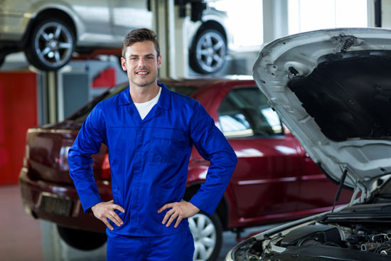 Portrait of smiling mechanic standing with hands on hip in repair shop